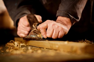 Senior man or carpenter doing woodworking planing the surface of a plank of wood in his workshop with a manual plane as he enjoys his creative hobby